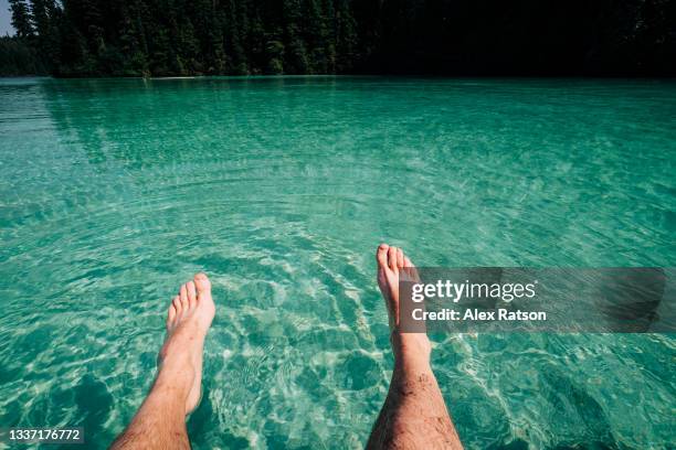 pov shot of man sitting on edge of turquoise coloured lake - feet on table stock pictures, royalty-free photos & images