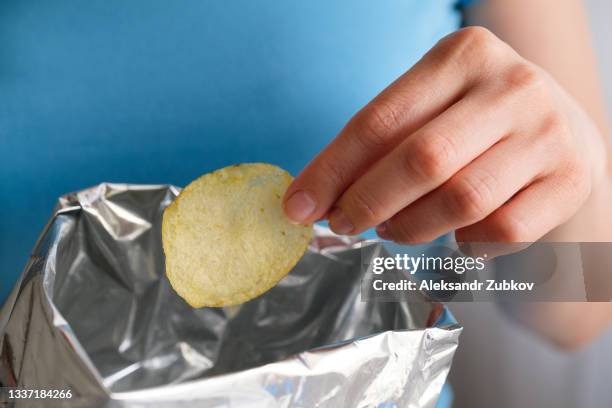 the girl takes crispy fried fatty potato chips from a package or pack. chips in the hands of a woman, she eats them. the concept of an unhealthy diet and lifestyle, the accumulation of excess weight. - crisps stock pictures, royalty-free photos & images