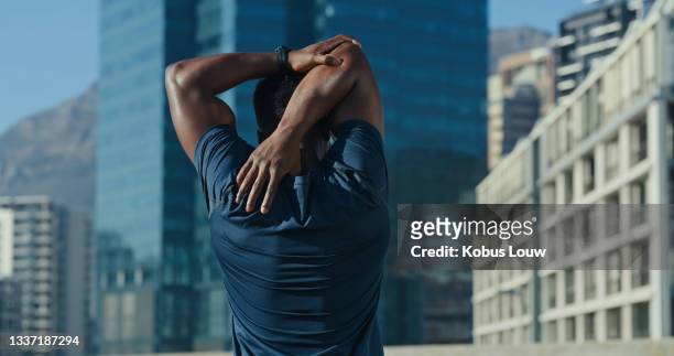 shot of a sporty young man stretching his arms while exercising outdoors - back stretch stock pictures, royalty-free photos & images