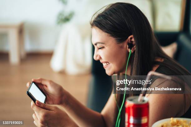 girl watching video on smartphone with can of juice and popcorn - broadcasting house stock pictures, royalty-free photos & images