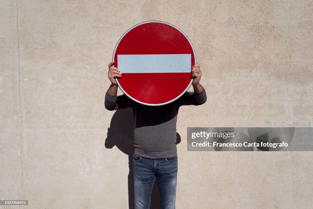 Man covering her face with a no entry sign