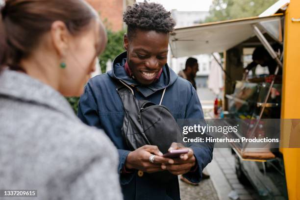 guy smiling while messaging on smartphone in food truck queue - food truck street stock pictures, royalty-free photos & images