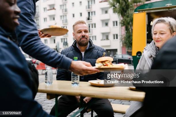 food truck owner serving burgers to customers sitting at tables - food truck street stock-fotos und bilder