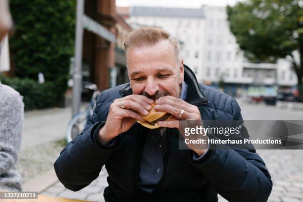 man enjoying burger from food truck outdoors - eating fast food stock-fotos und bilder