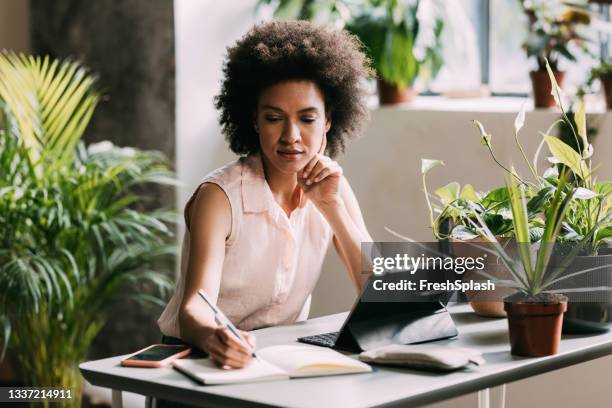 pensive mid adult mixed race businesswoman working in her home office - environmental conservation stock pictures, royalty-free photos & images