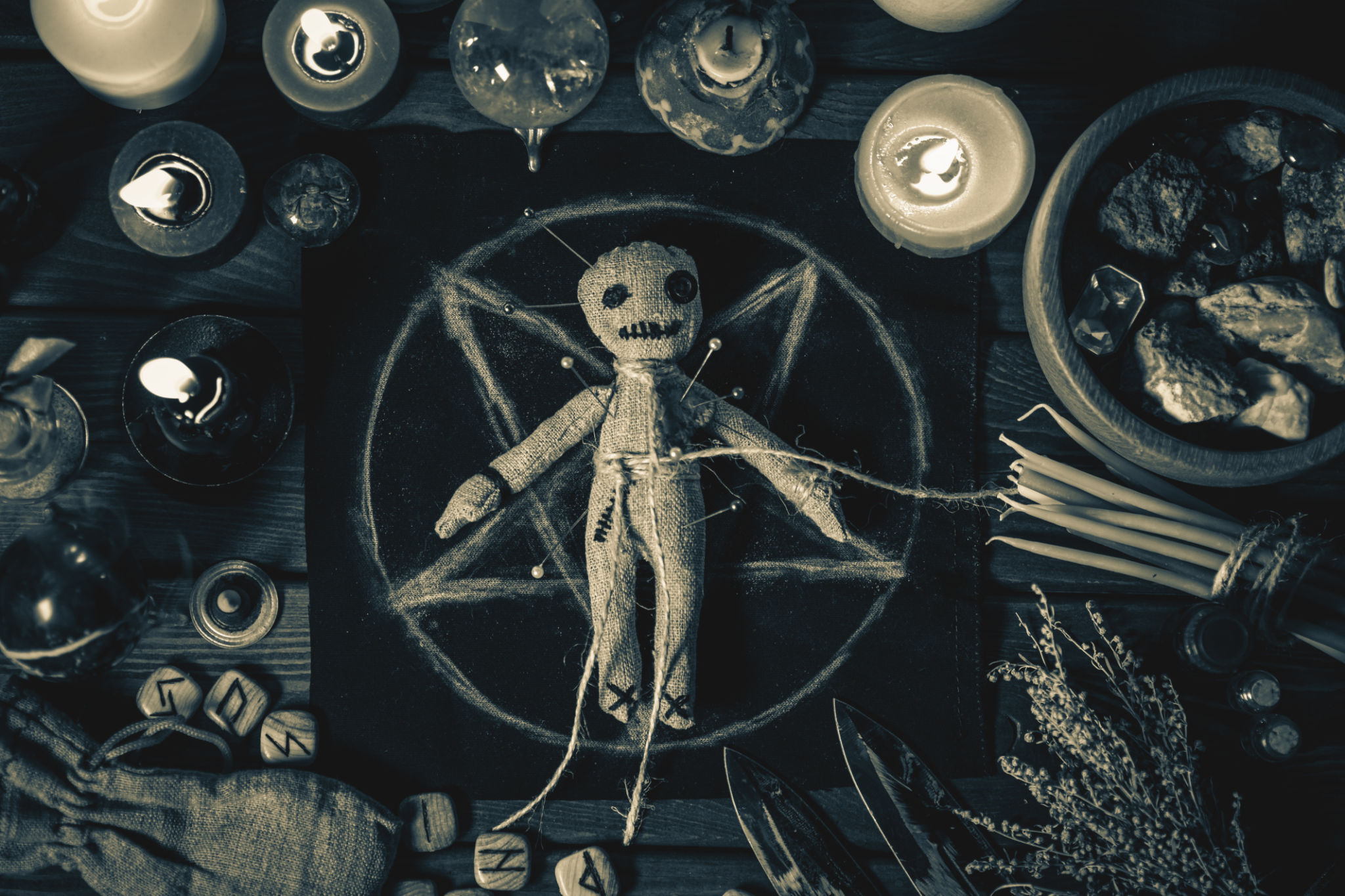 Voodoo Magic concept. Voodoo doll studded with needles with pierced rag heart on pentagram and around burning candles. Spooky or eerie magical esoteric ritual, black and white photo Voodoo Magic concept. Voodoo doll studded with needles with pierced rag heart on pentagram and around burning candles. Spooky or eerie magical esoteric ritual, black and white photo