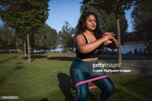 portrait of beautiful young overweight woman outdoors on riverbank in city,  doing exercise. - crouching stock pictures, royalty-free photos & images