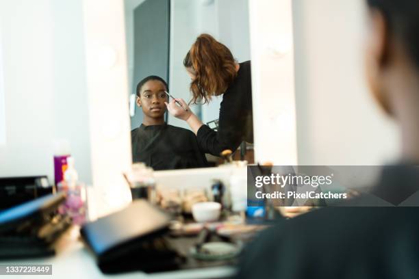 african model having make up applied backstage reflected in vanity mirror - visagist stockfoto's en -beelden