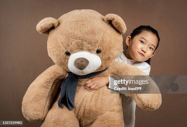 little girl embracing teddy bear on brown background - big hug stock pictures, royalty-free photos & images
