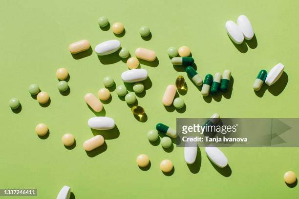 colorful pills and capsules on green background. minimal medical concept. flat lay, top view. - complément vitaminé photos et images de collection