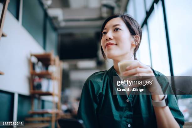young asian woman drinking a cup of coffee in cafe and looking away, enjoying life's simple pleasures - coffe shop stock-fotos und bilder