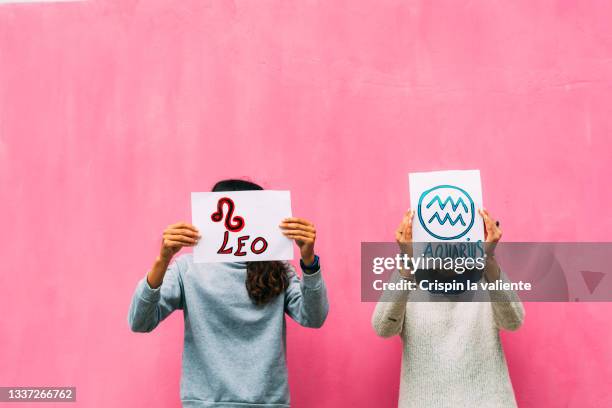 two people holding two signs of zodiac signs, taurus and aquariums, pink background - star signs fotografías e imágenes de stock