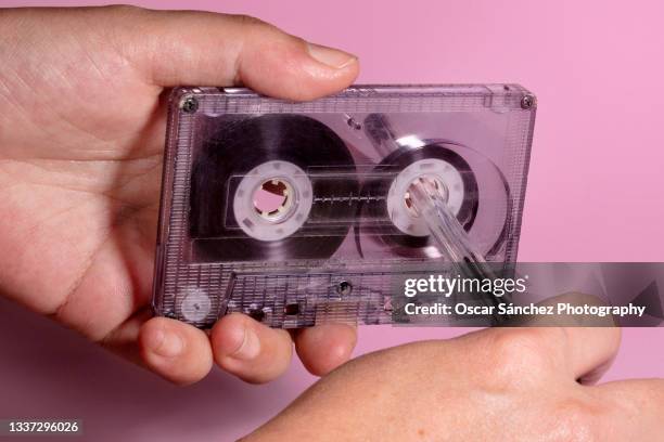 hand rewinding a cassette tape with a pen on pink background - stereo fotografías e imágenes de stock