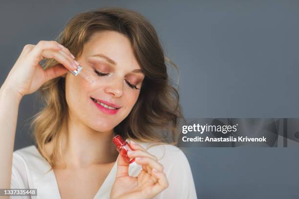 woman posing over grey background wall holding oil drop serum. - serum stock pictures, royalty-free photos & images