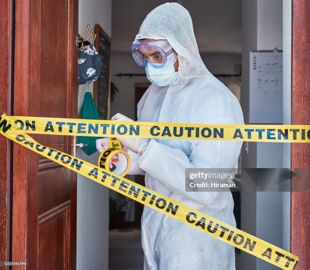 Shot of a worker in a protective suit cordoning off an area with barrier tape