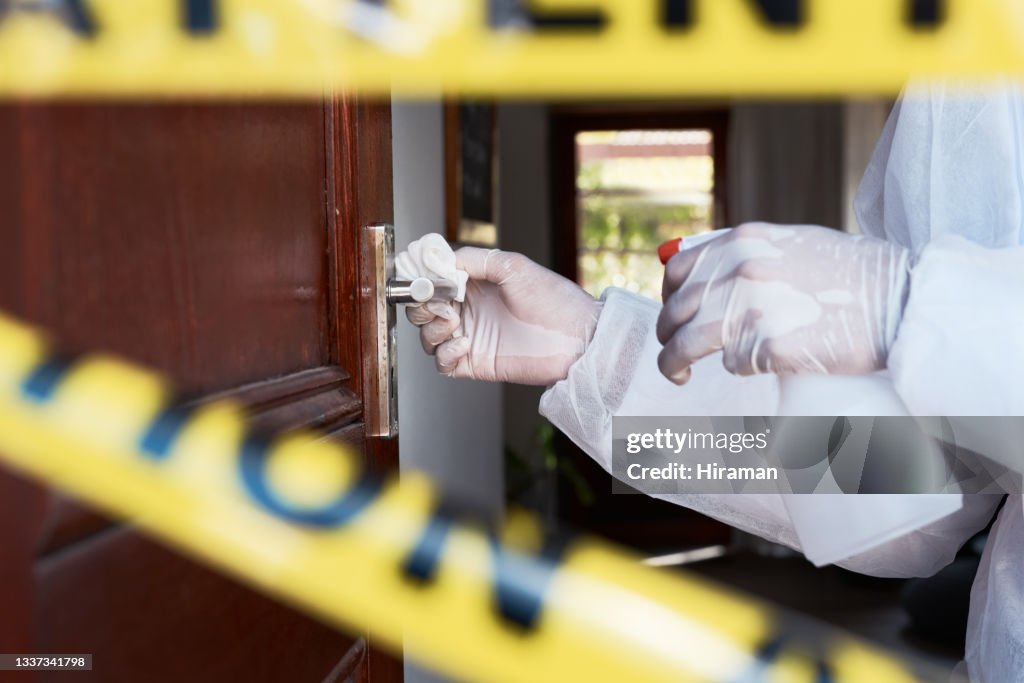 Closeup shot of an unrecognisable worker in a protective suit cleaning a doorknob in a cordoned off area