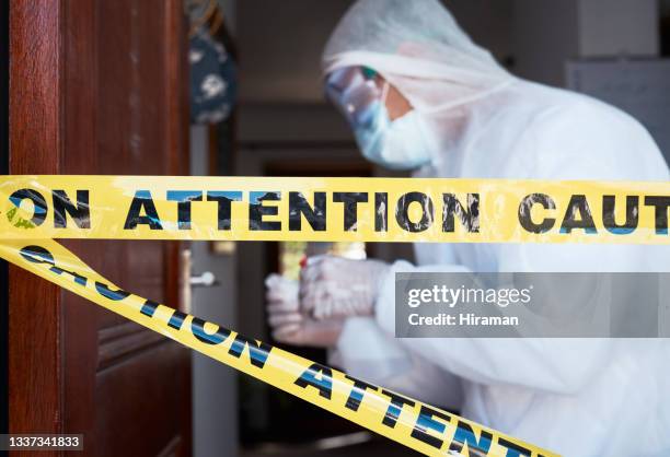 closeup shot of barrier tape across a doorway with a worker in a protective suit in the background - protective suit stock pictures, royalty-free photos & images