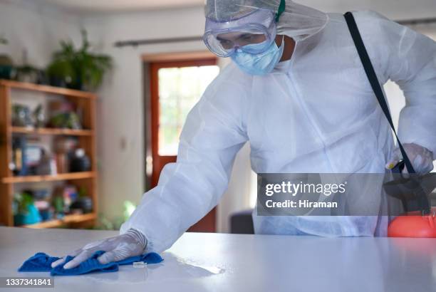 shot of a man in a hazmat suit cleaning a surface in a house - macacão de limpeza imagens e fotografias de stock