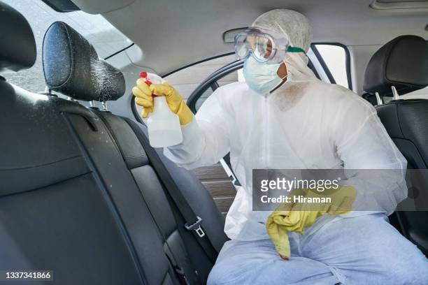 foto de un hombre con un traje de materiales peligrosos desinfectando un asiento en un automóvil - crime scene cleaners fotografías e imágenes de stock