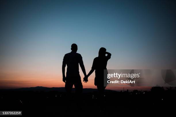 joven pareja enamorada tomándose de la mano y viendo la puesta de sol - love at first sight fotografías e imágenes de stock