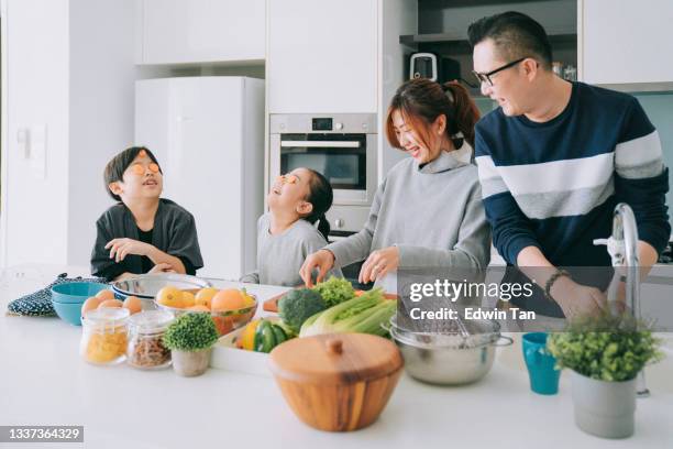 verspielte asiatische chinesische junge familie mit 2 kindern, die essen in der küche zubereiten und lustige zeit zusammen genießen - couples showering stock-fotos und bilder