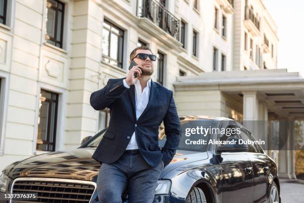 adult serious male businessman in a suit with a phone near the car on the background of a city street - car advertisement stock pictures, royalty-free photos & images