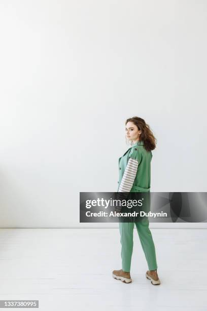 a woman in a green suit stands and looks at the camera on a white background in a room indoors with free space - man standing full body stock-fotos und bilder