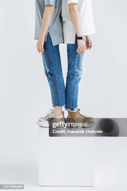 female legs of two models woman standing in new collection of casual clothes close-up in sneakers and jeans studio - high fashion stock-fotos und bilder