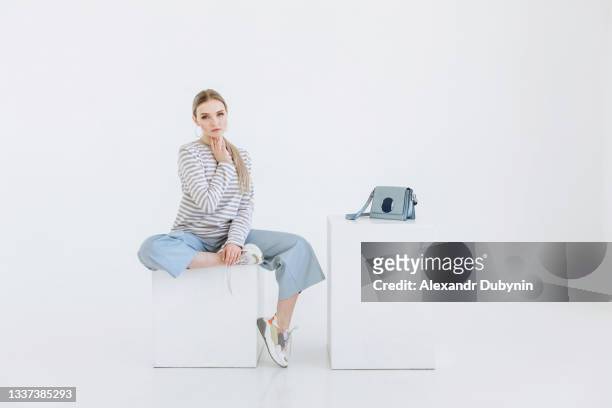 young woman model sitting in fashionable beautiful clothes on white background - white purse stock pictures, royalty-free photos & images