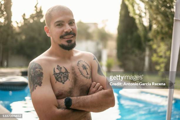 tattooed man poses next to his rustic home on a summer day - goatee stock pictures, royalty-free photos & images