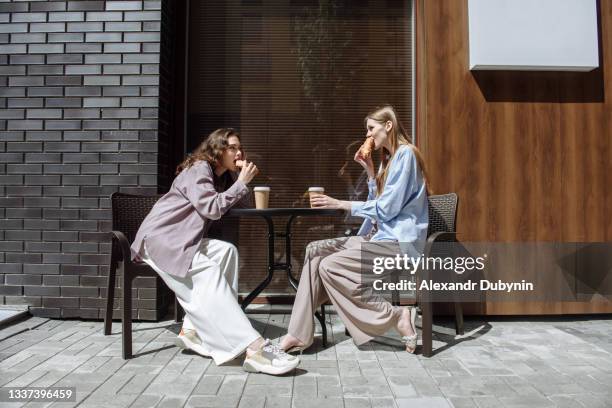 two young women sit in a cafe eating and chatting while having fun together - coffee shop chat imagens e fotografias de stock