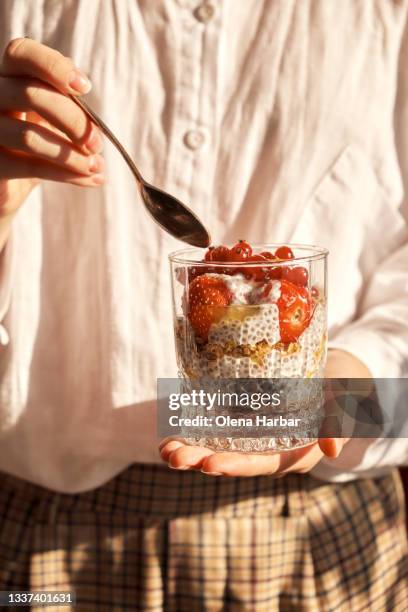 girl holding a small spoon and glass cup with vegetarian dessert in her hands - chiasamen stock-fotos und bilder