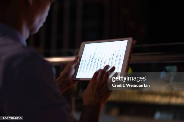 a man using a tablet at night, the tablet displays chart data - bilan photos et images de collection