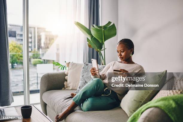 shot of a young woman using her card and phone to shop online at home - charging stockfoto's en -beelden