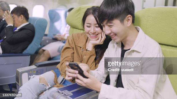 couple in flight looking at mobile phone - airplane seats stock pictures, royalty-free photos & images