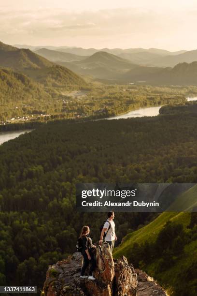 two young happy hikers man and woman with backpacks on the top of the mountain enjoy the view of the valley. travel and trip concept - woman sitting top man stock pictures, royalty-free photos & images