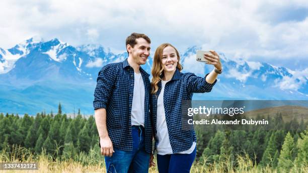 young couple of hikers man and woman take a selfie photo on the phone on their trip to the mountains on vacation. travel and adventure concept - russia travel stock pictures, royalty-free photos & images