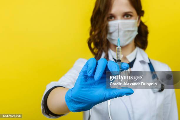 female doctor in mask and gloves with a syringe. coronovirus vaccine - surgeon holding needle stock-fotos und bilder