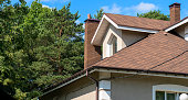 Close-up of asphalt shingled roofing construction with chimney, plastic soffit, fascia board and roof gutters installed
