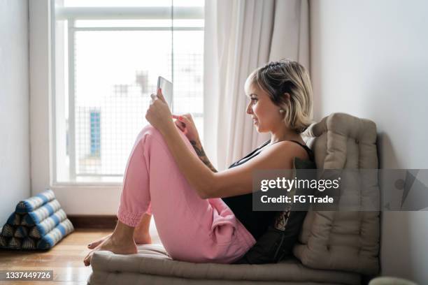 mujer sentada en un futón usando una tableta digital en casa - mala postura fotografías e imágenes de stock