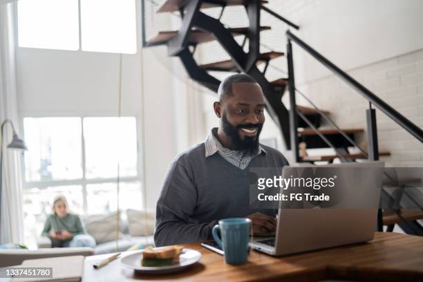 mid adult man using laptop working at home - mid adult men stock pictures, royalty-free photos & images