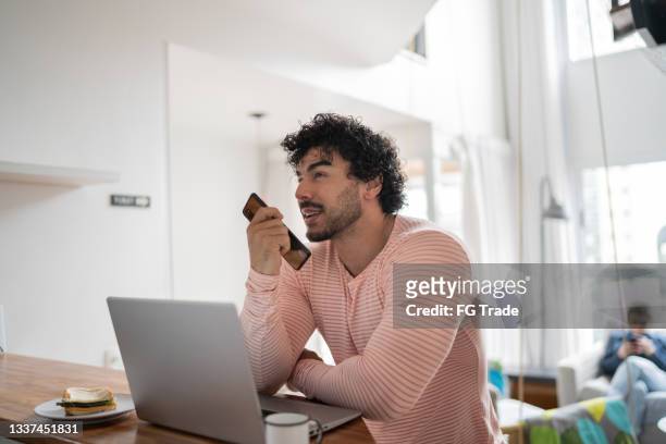 man using laptop and sending audio message on smartphone at home - speech recognition stock pictures, royalty-free photos & images