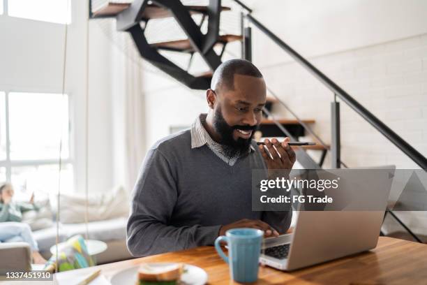 man using laptop and sending audio message on smartphone at home - diktera bildbanksfoton och bilder