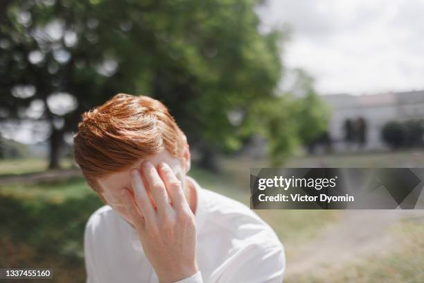 thoughtful redhead man in the white shirt in the sun - scham stock-fotos und bilder