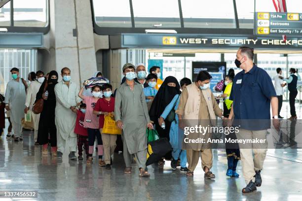 Refugees walk through the departure terminal to a bus at Dulles International Airport after being evacuated from Kabul following the Taliban takeover...