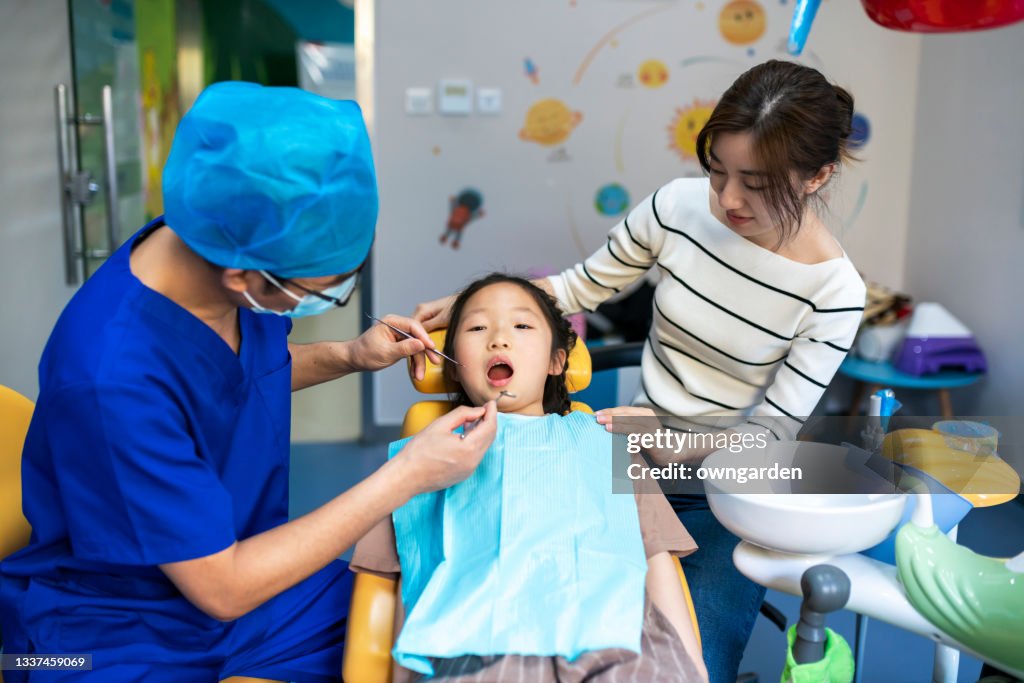 Dentist examining teeth of small girls teeth at dental clinic.