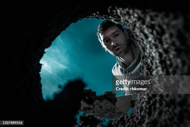 scared guy digging a deep earthen hole with a shovel during a moonlit night - vinden stockfoto's en -beelden