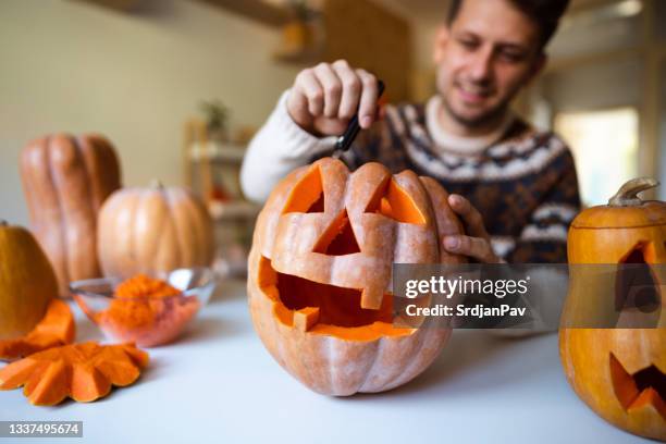 gutaussehender mann, der zu hause einen kürbis für halloween schnitzt - schnitzen stock-fotos und bilder