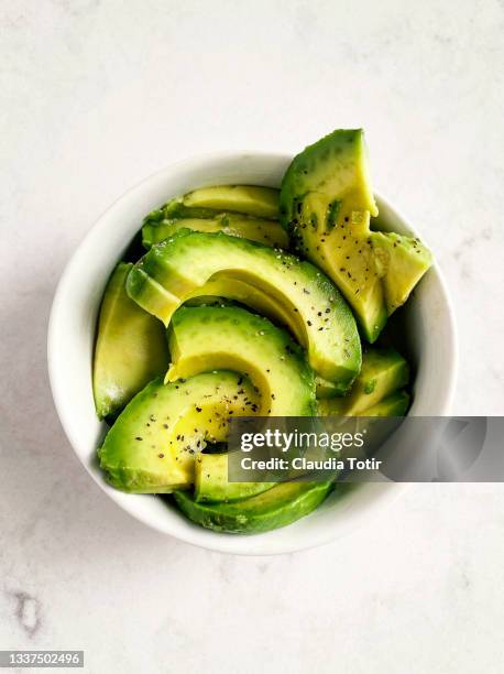 slices of fresh avocado in a bowl on white, marble background - avocado slices stock pictures, royalty-free photos & images