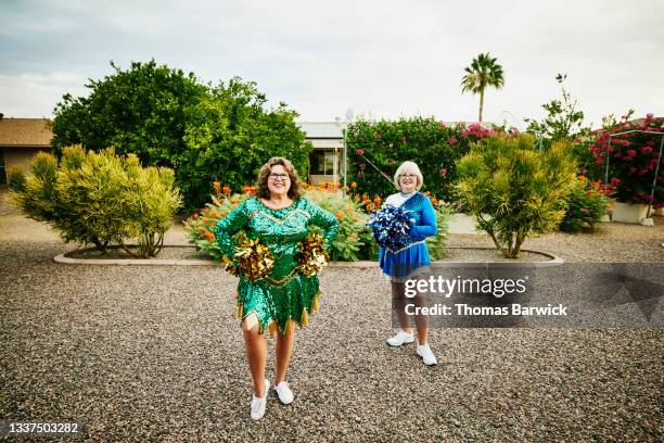 wide view portrait of smiling senior and mature female cheerleaders practicing in backyard - white pom pom stock pictures, royalty-free photos & images